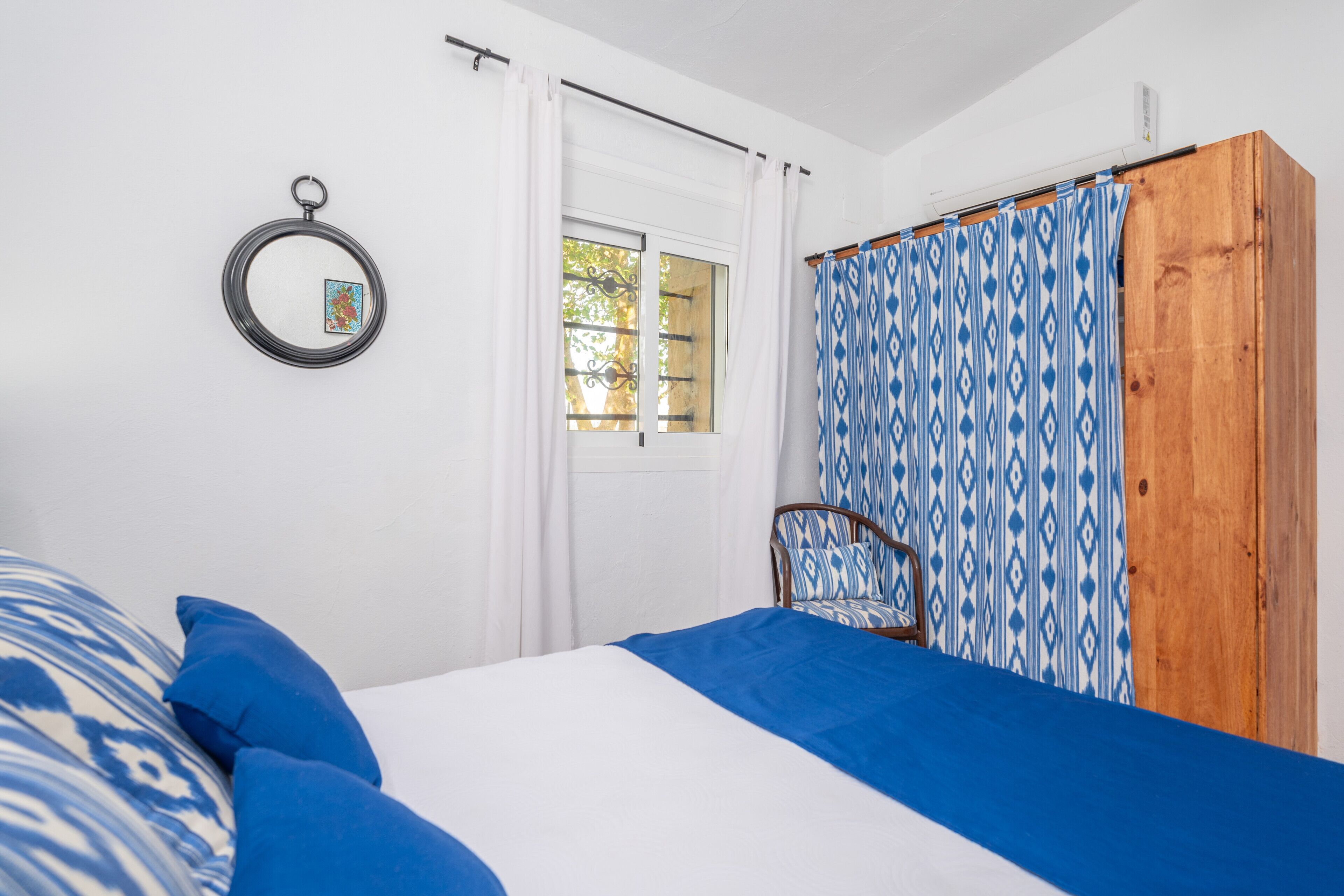 Un dormitorio con cama, una silla, una ventana y cortinas.