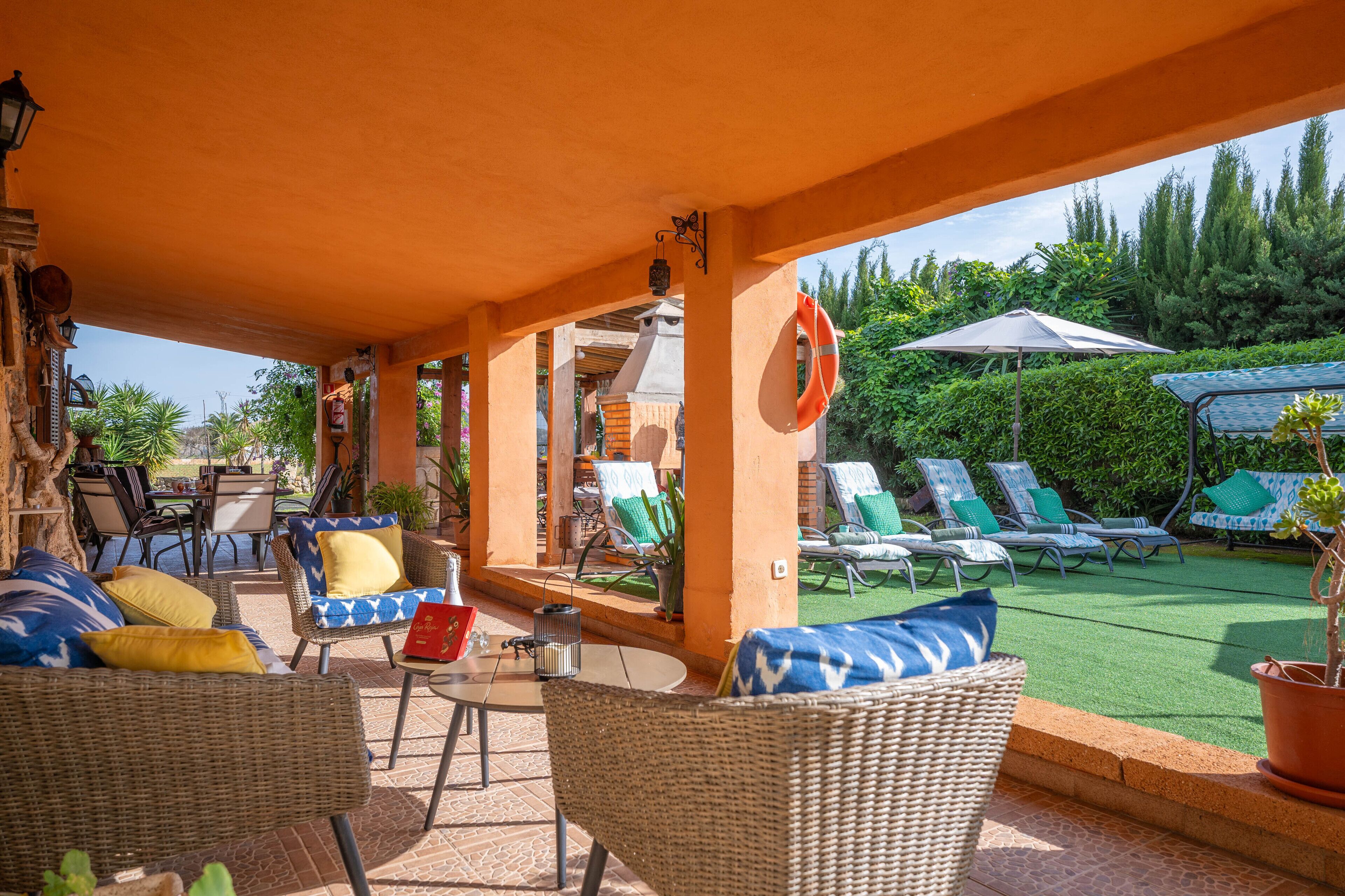 An outdoor patio with wicker furniture, a table, and a lawn area with lounge chairs and umbrellas.