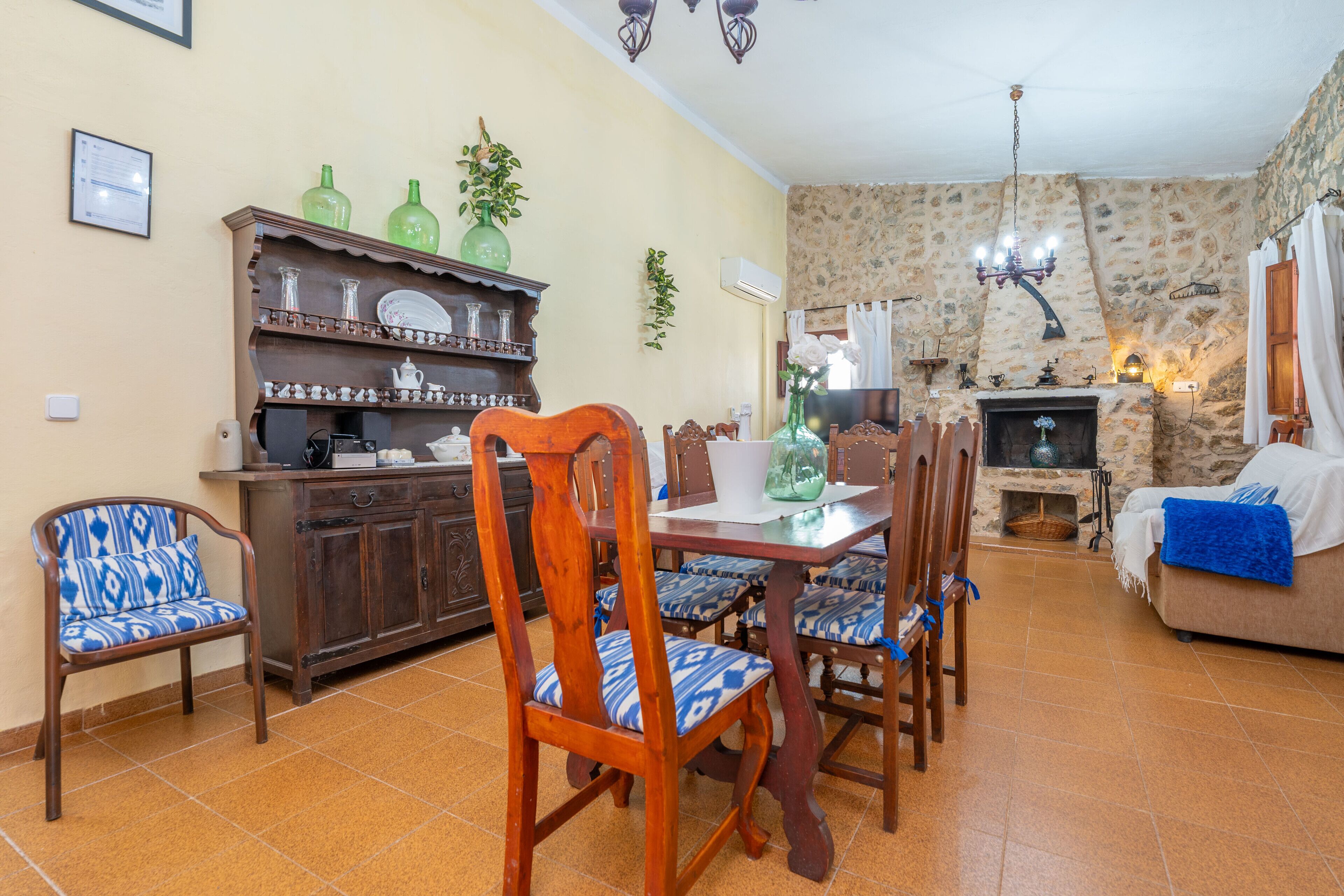 A dining area with a wooden table and chairs, a kitchen area with a wooden cabinet, and a stone wall with a fireplace.
