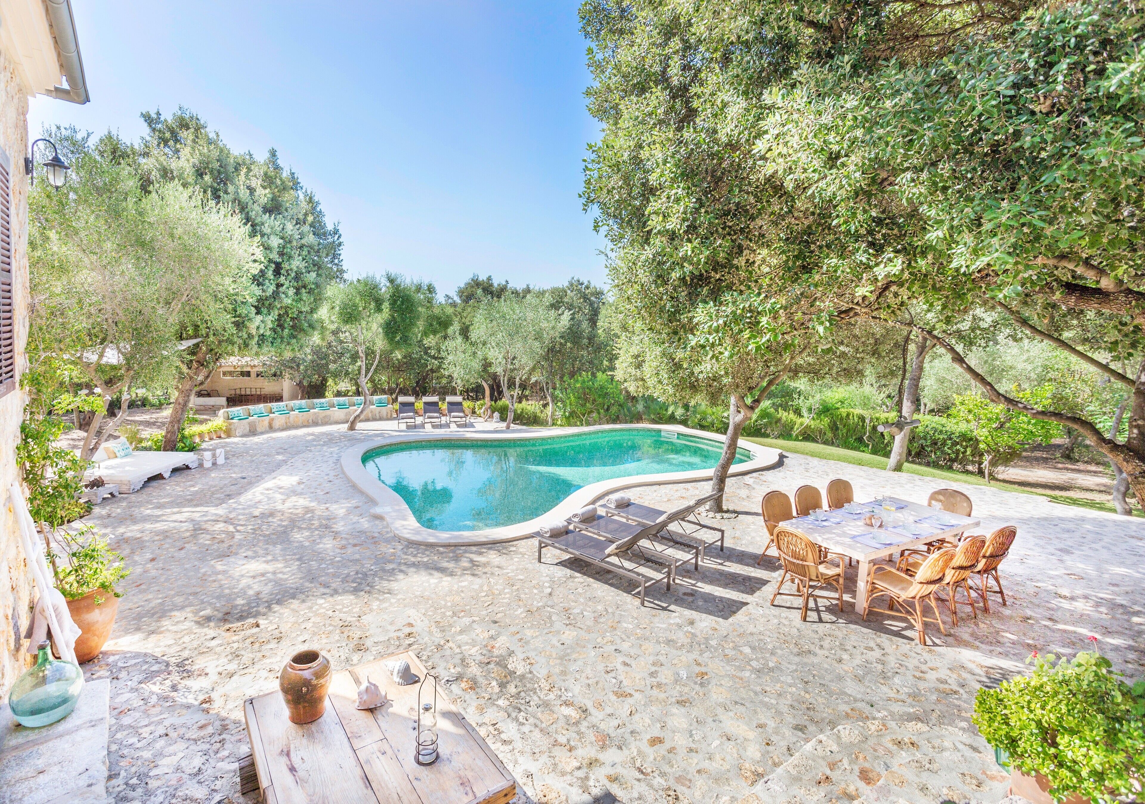 A swimming pool surrounded by lounge chairs and a table, with trees and a building in the background.