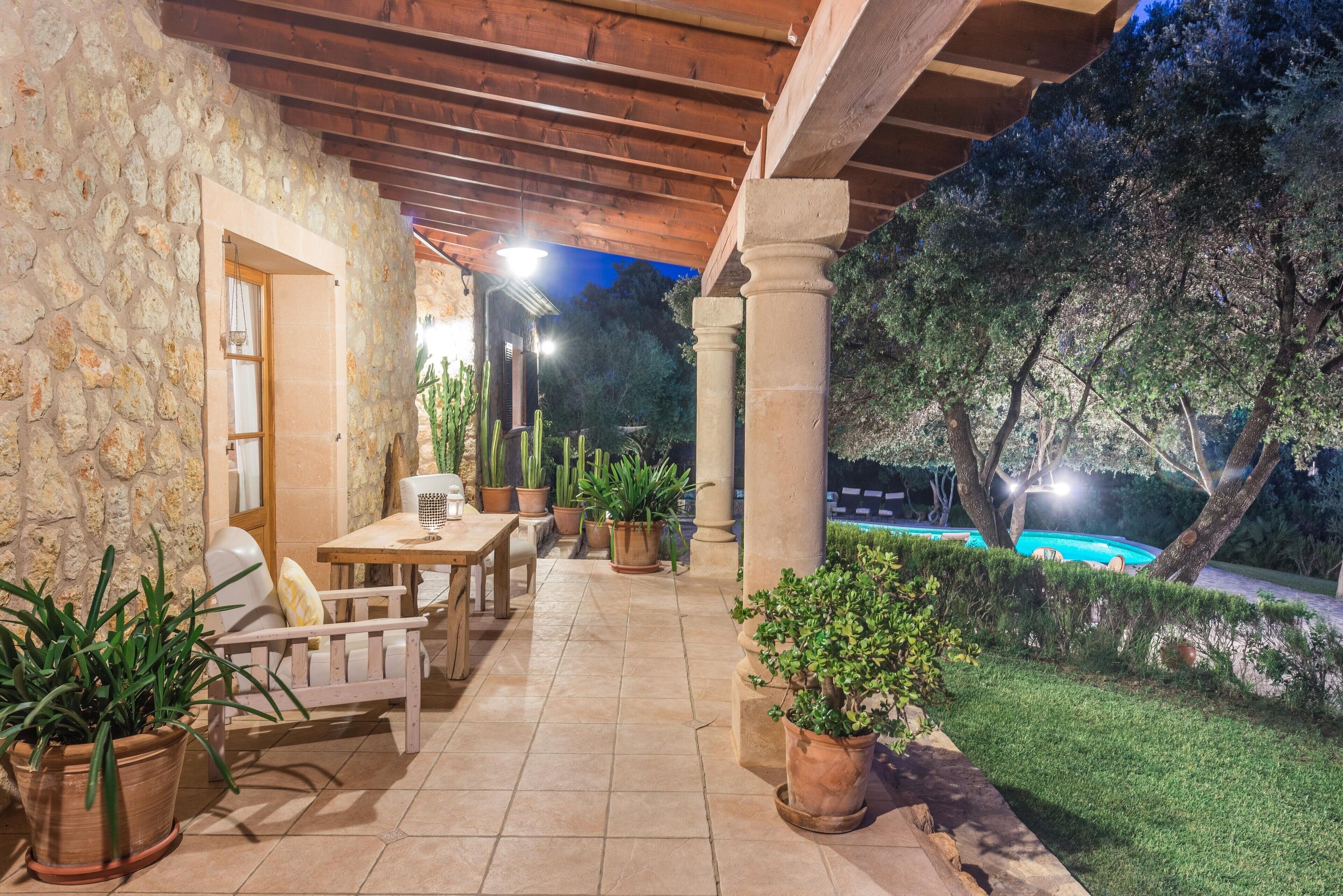 An outdoor patio with stone walls, wooden furniture, and potted plants.