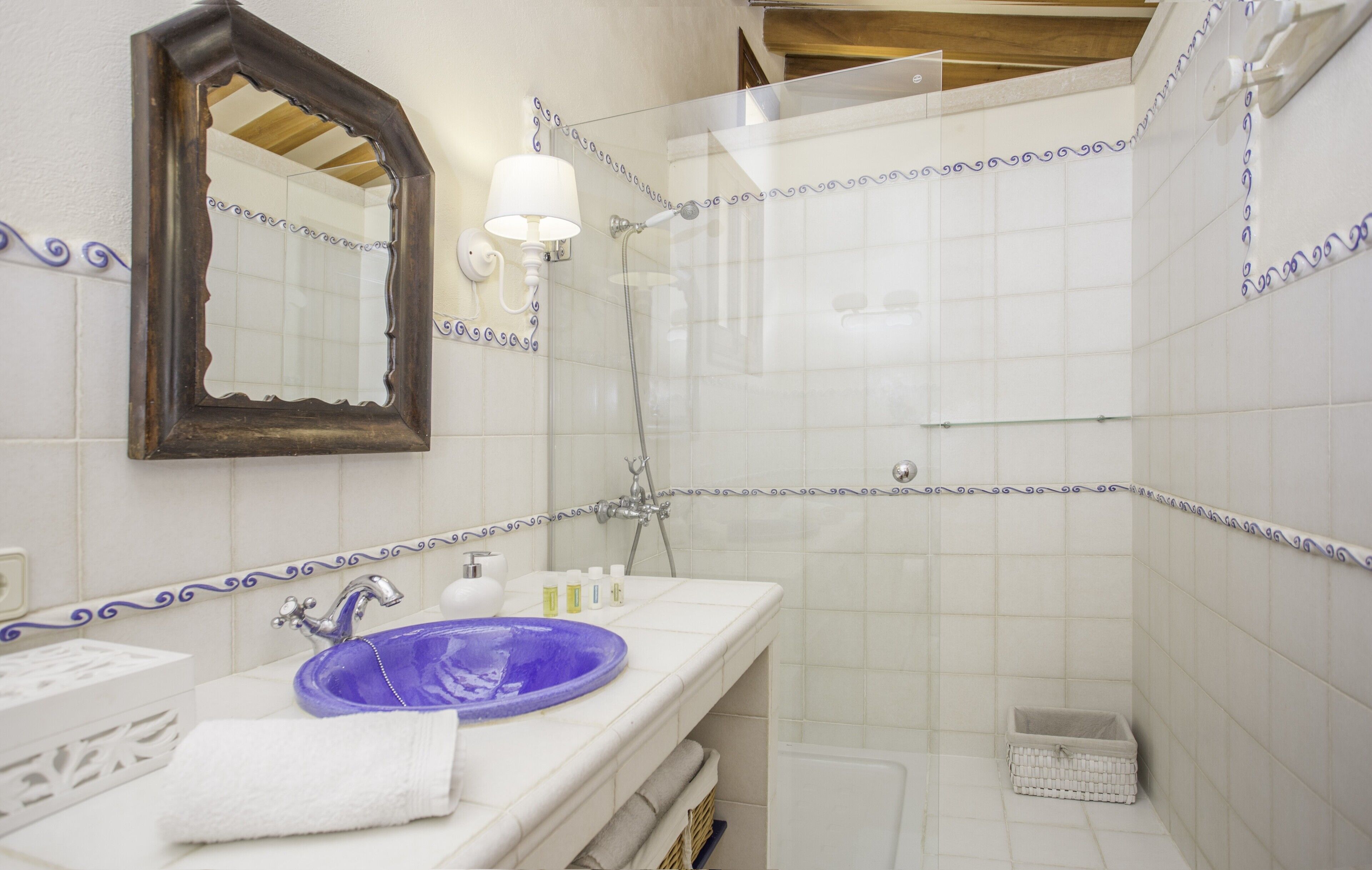 A bathroom with a large mirror, a purple sink, a shower, and a white tiled wall with decorative borders.