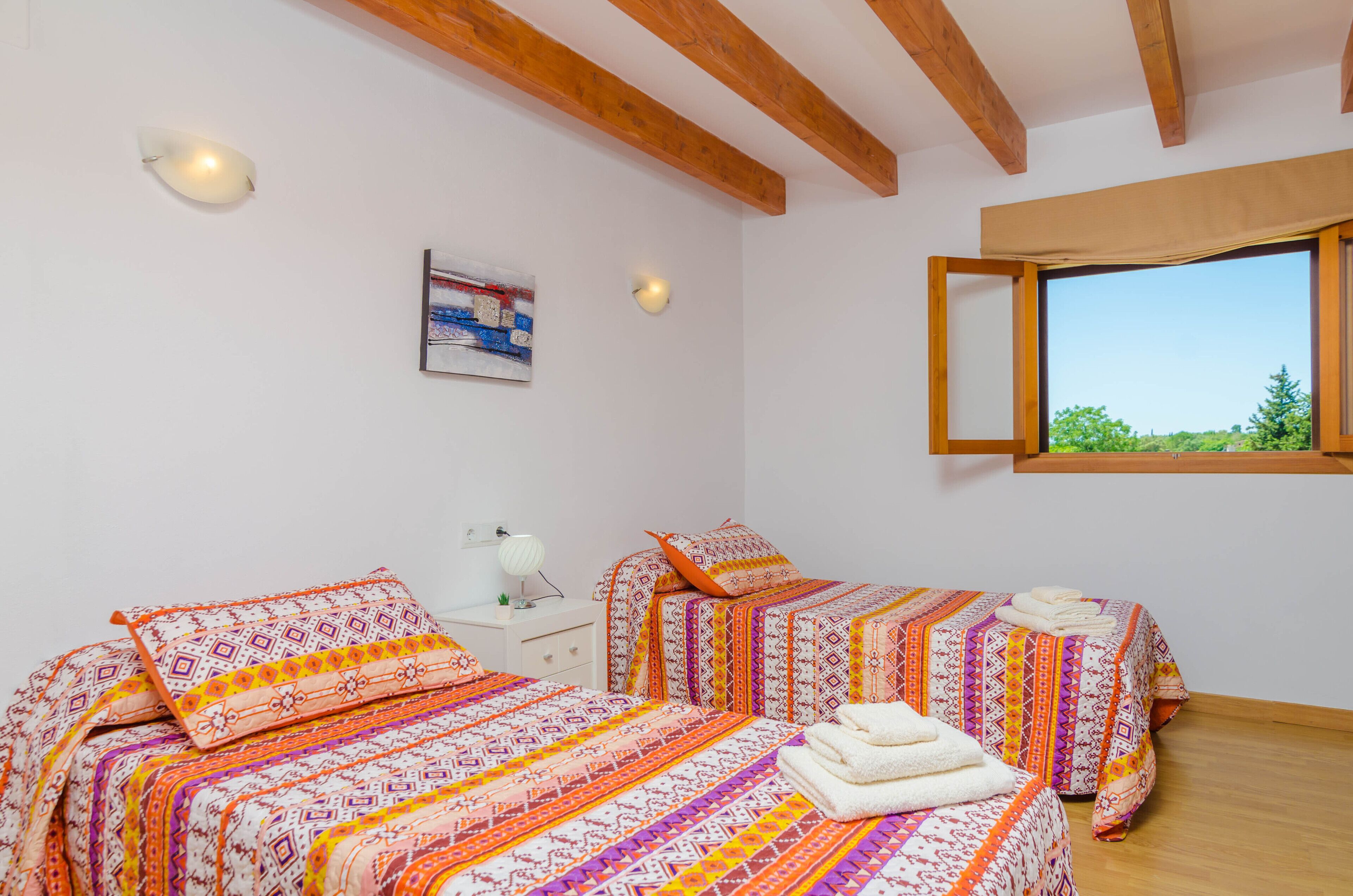 A bedroom with two beds, a nightstand, a lamp, and a window with a view.