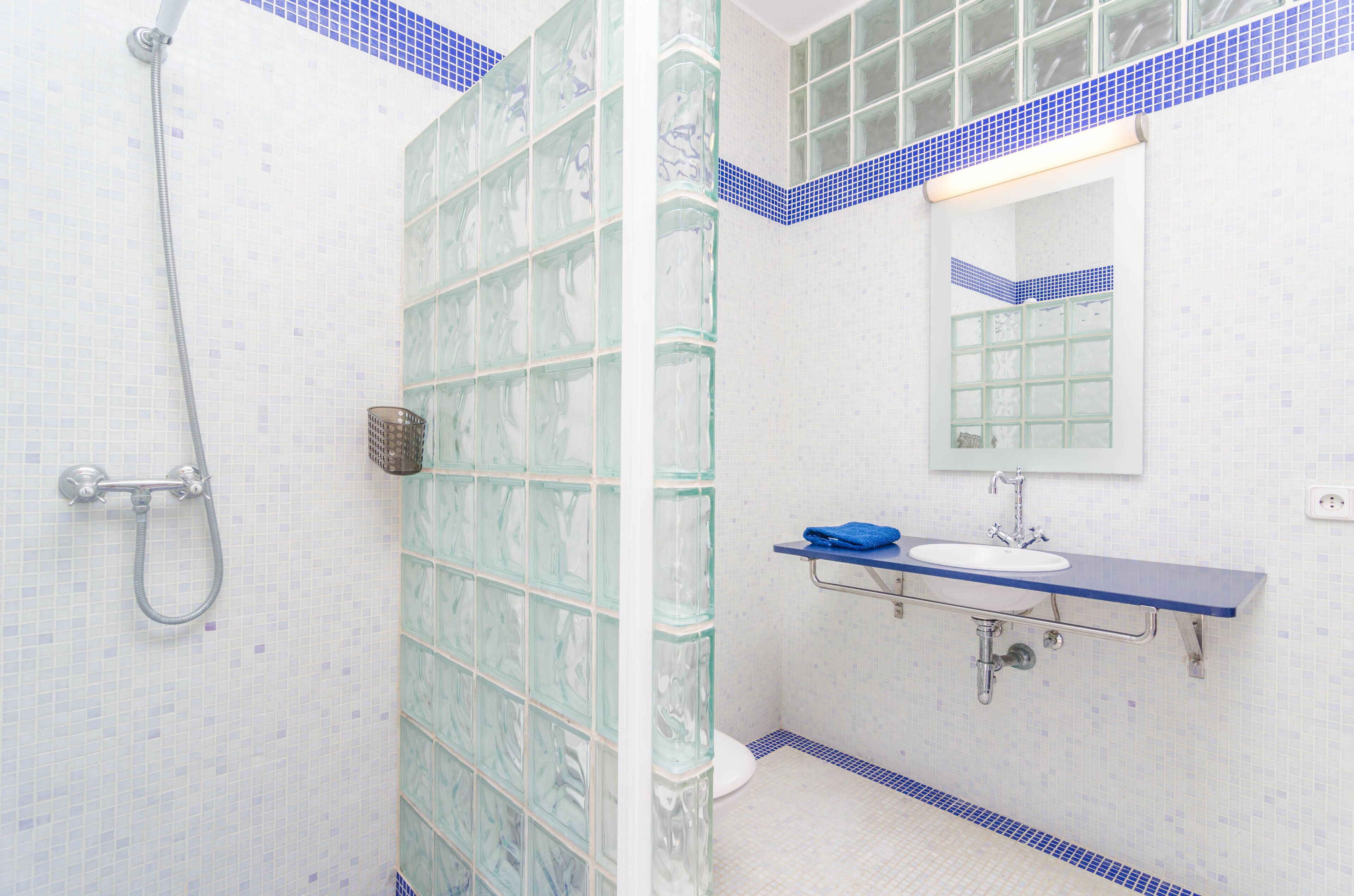 A bathroom with a glass shower enclosure, a white toilet, a sink with a blue countertop, and a mirror above the sink.