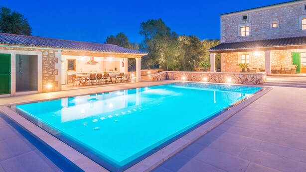 Una piscina con area coperta e posti a sedere all'aperto, circondata da edifici in pietra con finestre e porte.