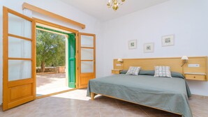 Una camera da letto con un letto, un comodino, una lampada, una testiera in legno e un'ampia finestra con persiane verdi.