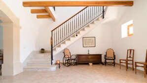 Una scala con ringhiera in legno e balaustre in metallo, che porta a un pianerottolo con un armadietto in legno e due sedie in vimini.