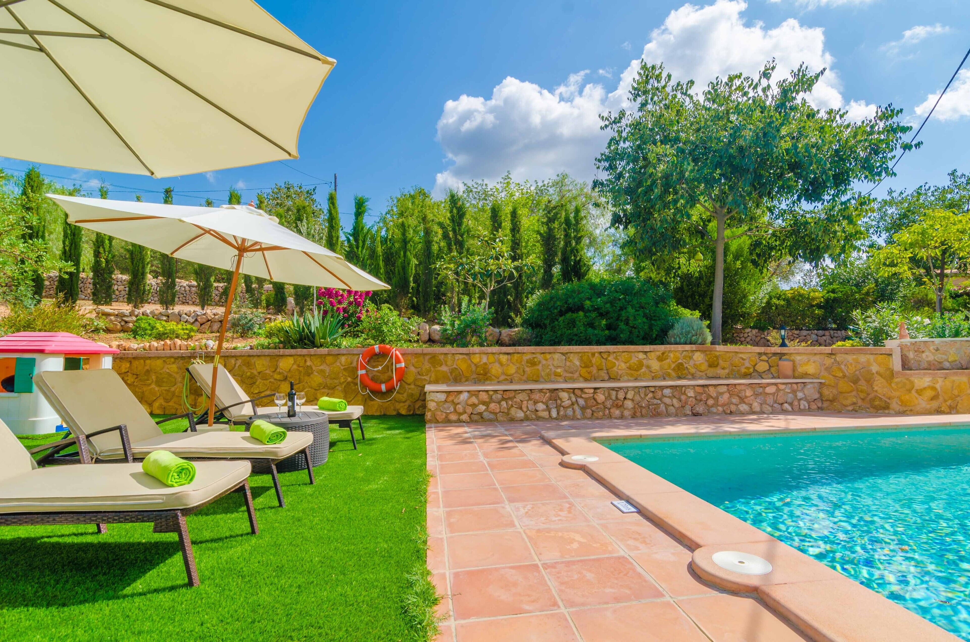 A poolside area with lounge chairs, a large umbrella, and a stone wall.