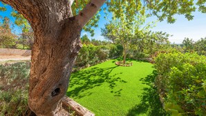 Un jardin bien entretenu, agrémenté de divers arbres et arbustes, avec une pelouse soigneusement taillée et un mur de pierres en arrière-plan.