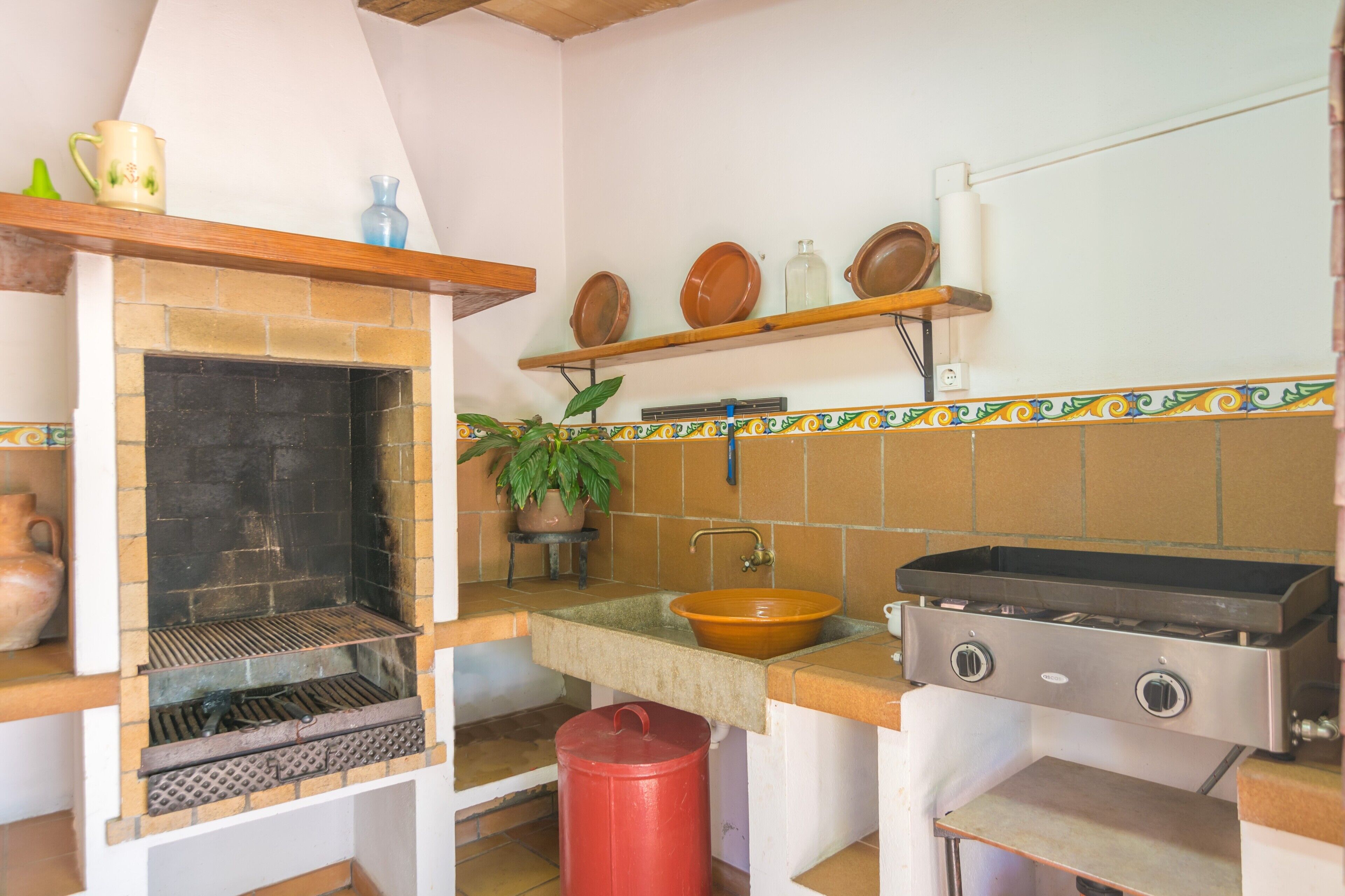A kitchen with a built-in grill, a sink, and a shelf with dishes.