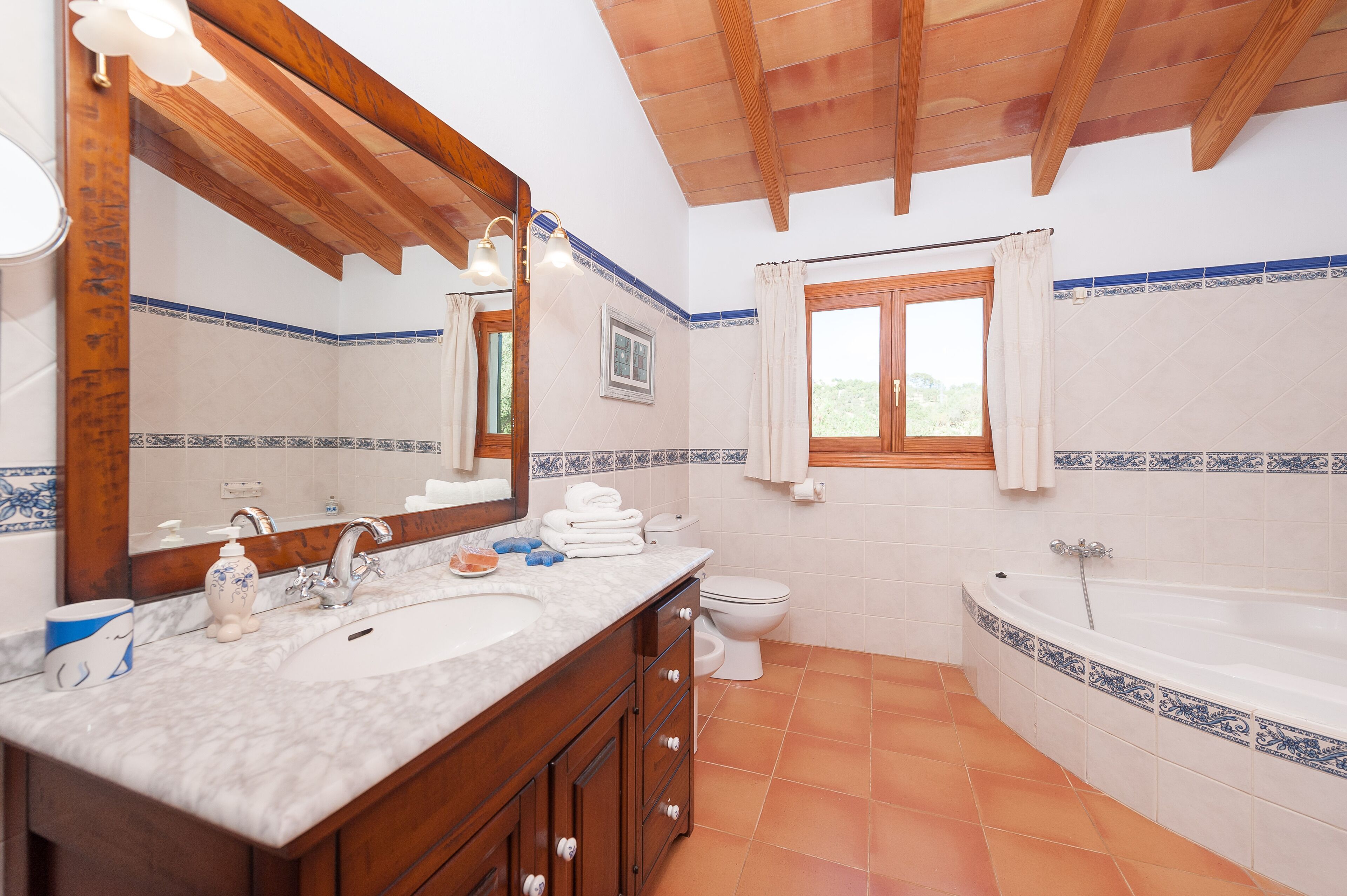 Un baño con techo de madera, un espejo grande, un lavamanos, un inodoro y una bañera.