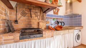 A kitchen with a brick wall, a grill, hanging utensils, and a washing machine.