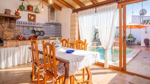 A dining area with a table and chairs, a kitchen with hanging pots, and a pool outside.