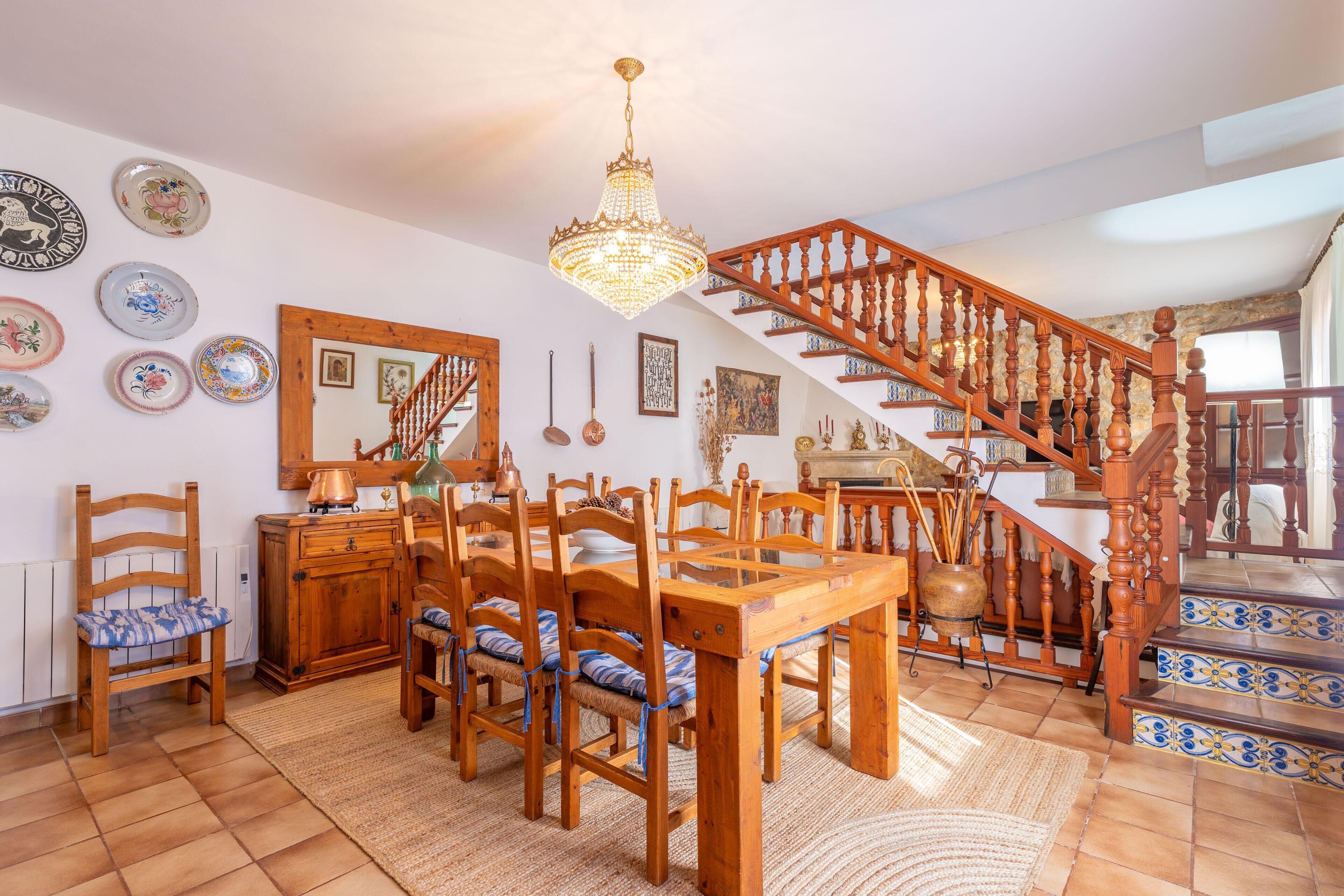 Un espace repas avec des meubles en bois, un lustre et un escalier orné de carreaux bleus et blancs.