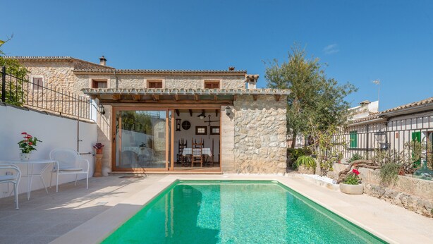 A stone building with a pool, outdoor seating, and a covered patio area.