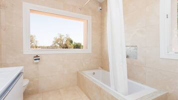 Une salle de bain avec une baignoire, une fenêtre et un carrelage au sol.