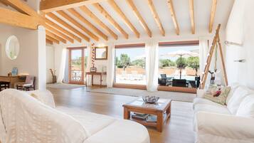 Un salón amplio con vigas de madera, muebles blancos y vistas al exterior.