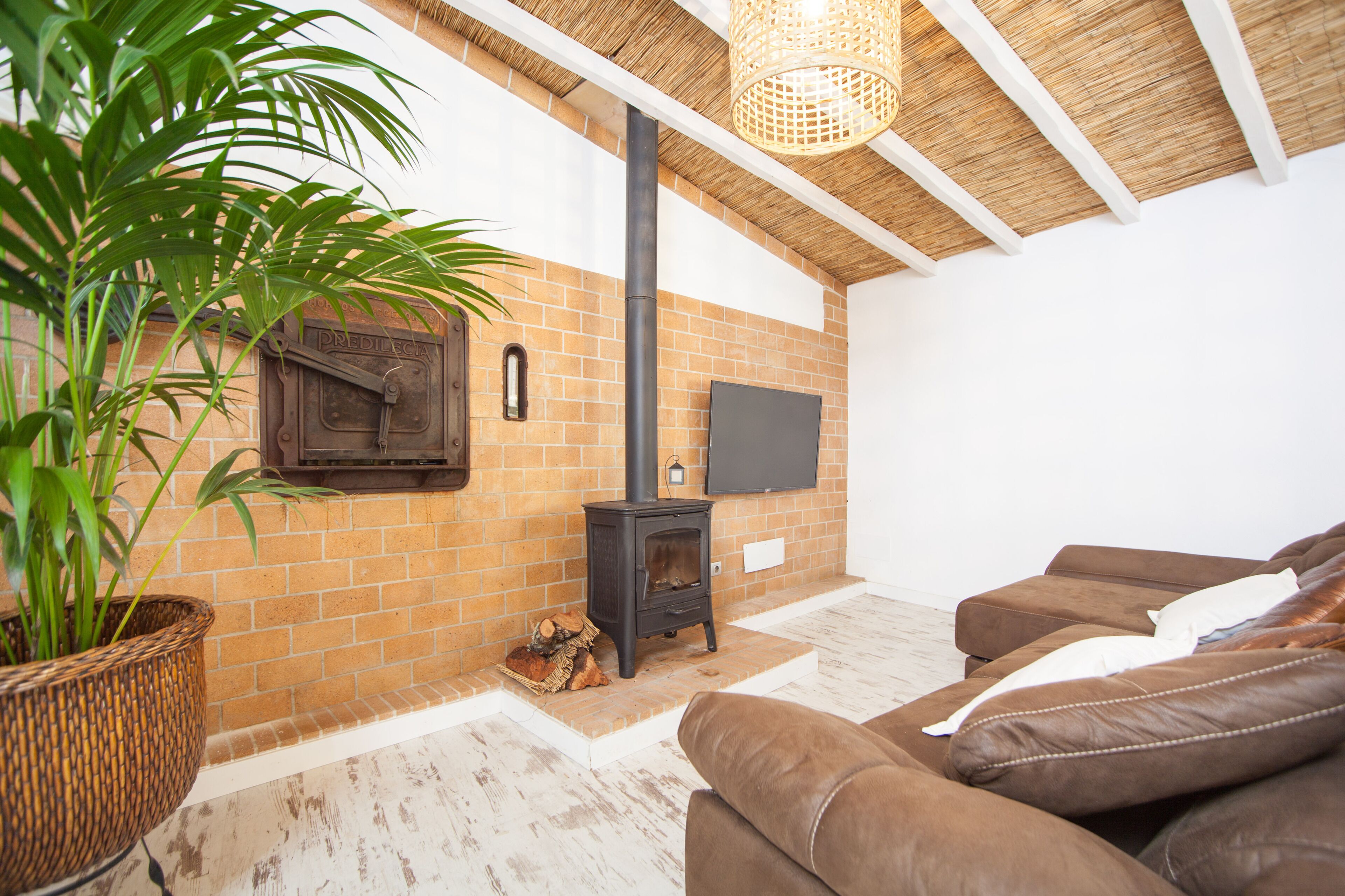 A cozy living room with a brick fireplace, a flat-screen TV, and a large brown leather sofa.