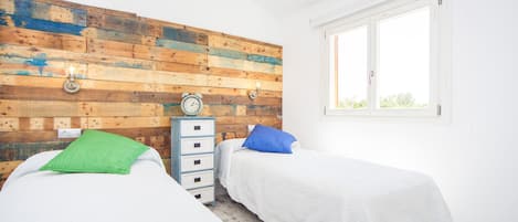 A bedroom with two beds, a wooden wall panel, a clock, a dresser, and a window.