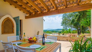An outdoor dining area with a wooden table and white chairs, a bottle of wine, and a bowl of fruit. - SON MORA - Villa with private pool in Porreres. Free WiFi (Porreres)