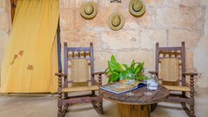 Una habitación rústica con una mesa de madera, dos sillas de madera, un cortinón amarillo y tres sombreros de paja en la pared.