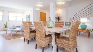 Un coin repas avec des chaises en osier, une table blanche et des lampes suspendues.