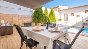 Un espace de restauration en plein air avec une table dressée pour deux personnes, entouré de meubles en osier et avec une piscine en arrière-plan.