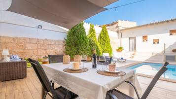 An outdoor dining area with a table set for two, surrounded by wicker furniture and a pool in the background.