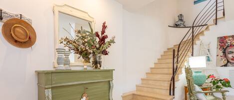 A staircase with a wooden finish, a green dresser with decorative elements, a rocking chair, and a mirror with a floral arrangement.