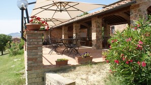 Une terrasse extérieure avec des murs en pierre, une table et des chaises, et un grand parasol pour faire de l’ombre.