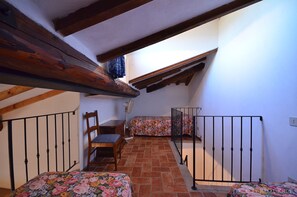 A small, cozy room with a sloped ceiling, wooden beams, a bed with a floral bedspread, a chair, and a small table.