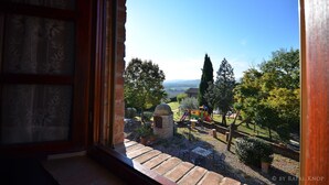 Une vue depuis une fenêtre donnant sur un jardin avec un espace de jeux, des structures en pierre et des arbres.