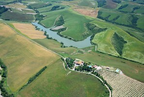 An aerial view of a rural landscape with fields, a river, and a small settlement with buildings and a swimming pool.