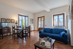 Cozy living space with a large sofa, dining table, and TV, surrounded by framed pictures and large windows.
