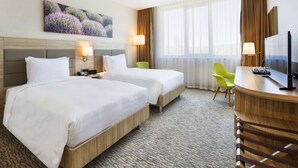 A hotel room with two beds, a desk, a chair, a TV, and a painting on the wall. - Hilton Garden Inn Isparta (Isparta)