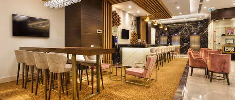 Een moderne hotellobby met een bar, zitplaatsen en een marmeren receptiebalie.