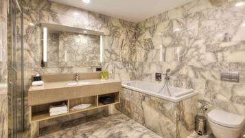 Un baño moderno con suelo y paredes de mármol, ducha con cerramiento de vidrio, tocador con lavabo y espejo, y un inodoro.