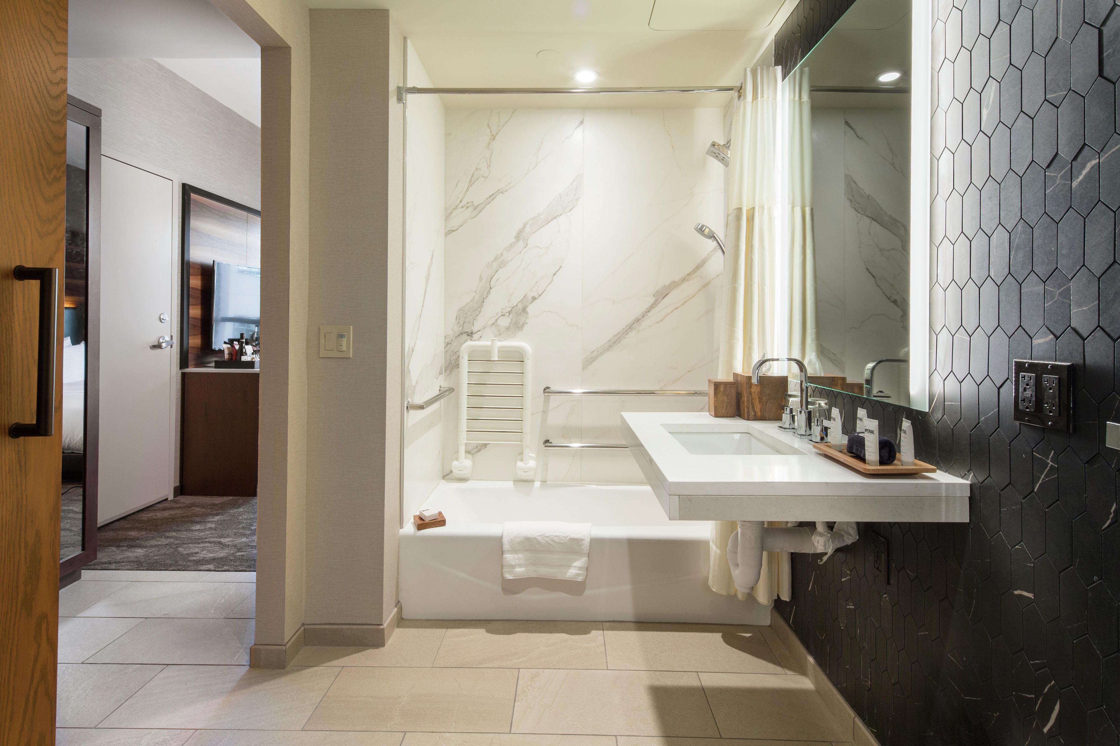 A modern bathroom with a marble shower, a large mirror, and a black hexagonal tile wall.