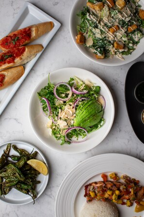 A variety of dishes including a salad with lettuce and red onions, a plate of rice with mango salsa, and grilled fish. - The Porter Portland, Curio Collection by Hilton (Portland)