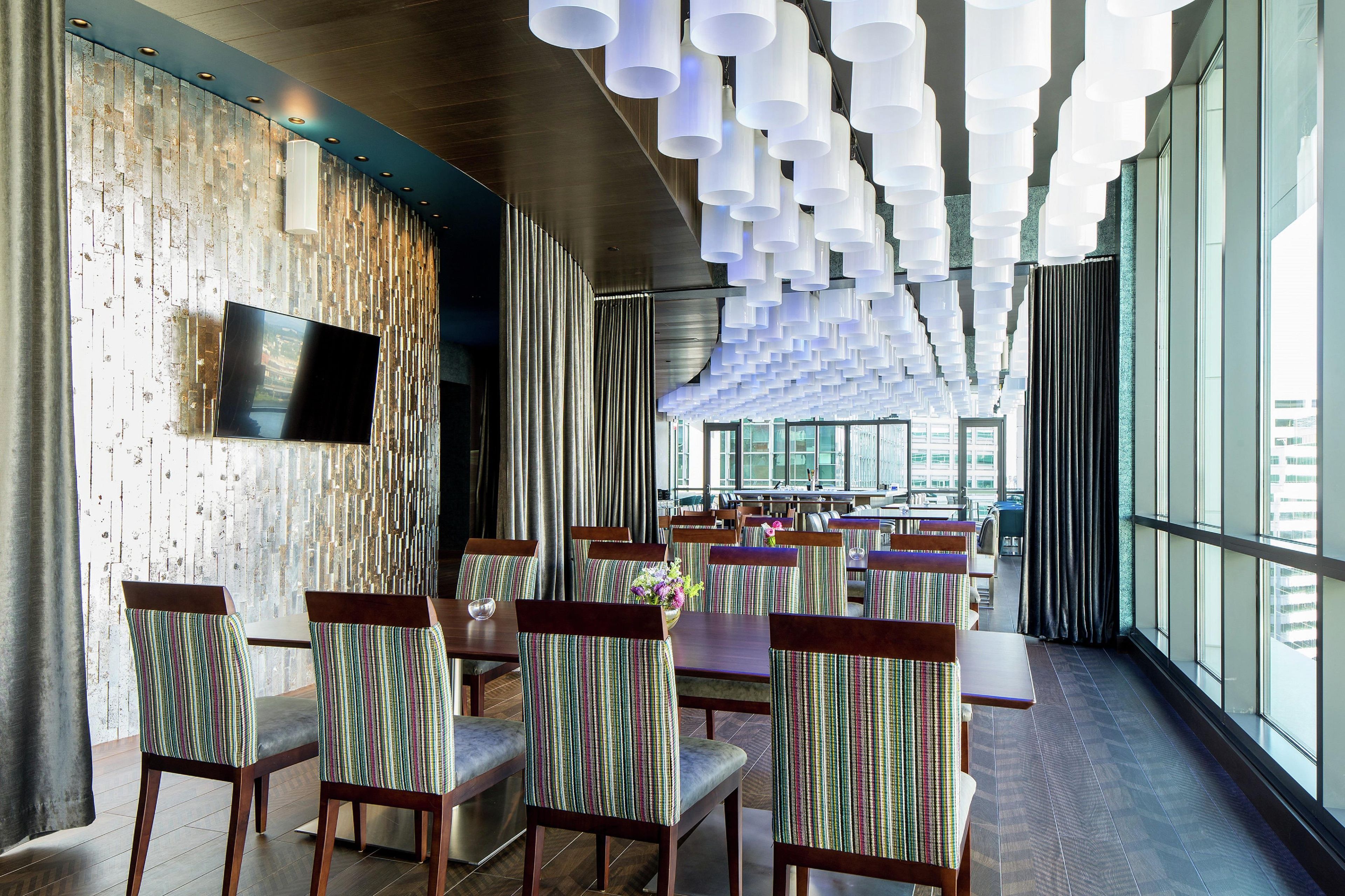 Un espace de repas moderne avec des murs en bois, un téléviseur à écran plat et un plafond orné de lampes blanches suspendues.