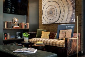 A cozy reading nook with a leather couch, a bookshelf, and a large wall art piece. - The Porter Portland, Curio Collection by Hilton (Portland)