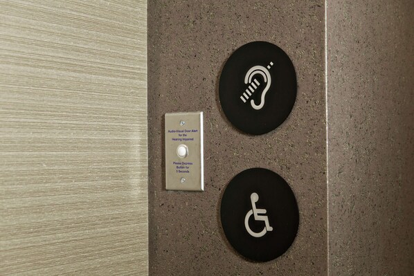 A tactile floor indicator and a hearing impaired alert button on a textured wall.