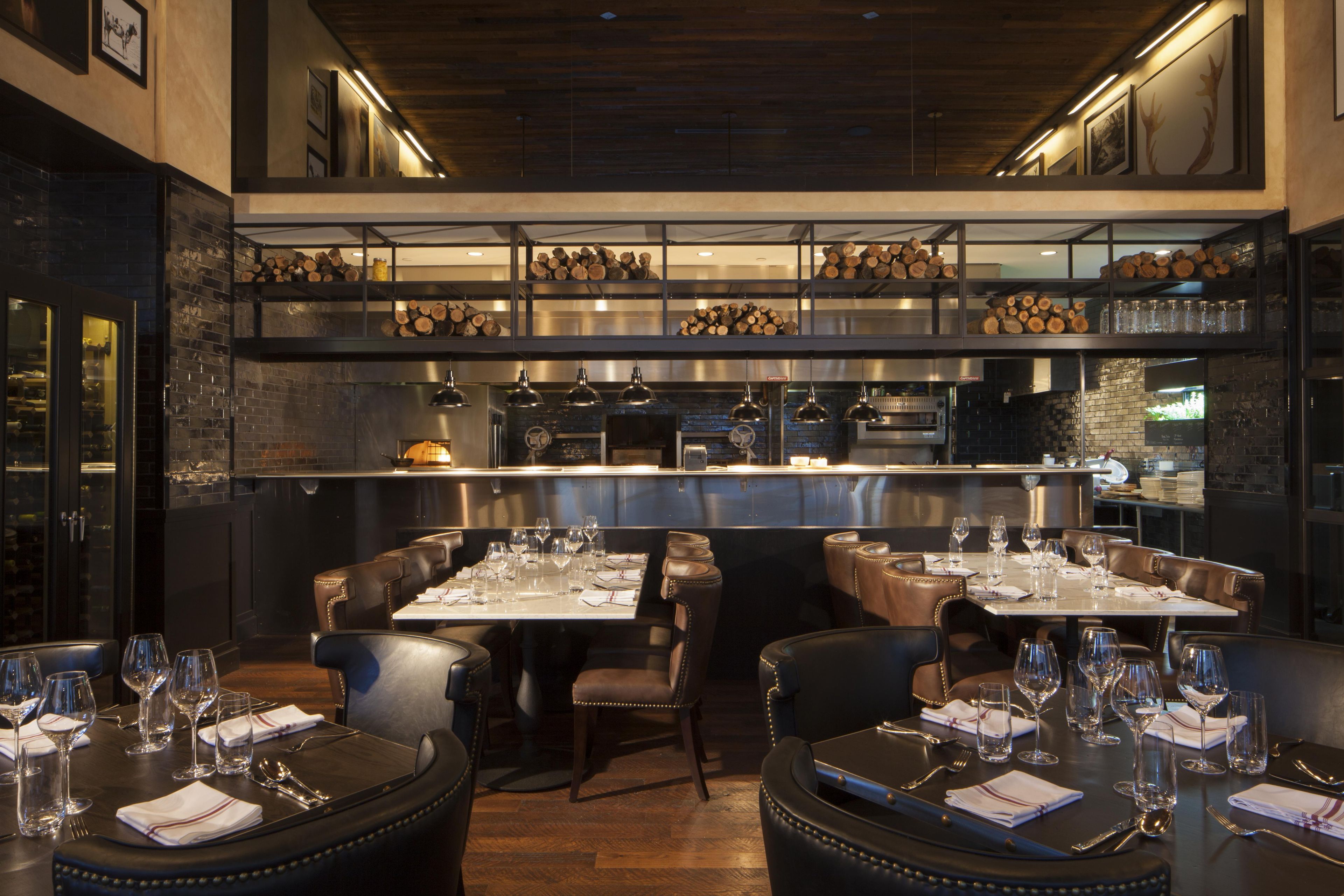 A restaurant interior with high tables, leather booths, and a kitchen in the background.