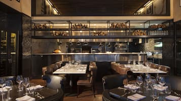 A restaurant interior with high tables, leather booths, and a kitchen in the background.