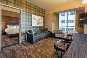 Une chambre d’hôtel comprenant un lit, un canapé, une table à manger avec des chaises, une télévision et une grande fenêtre.