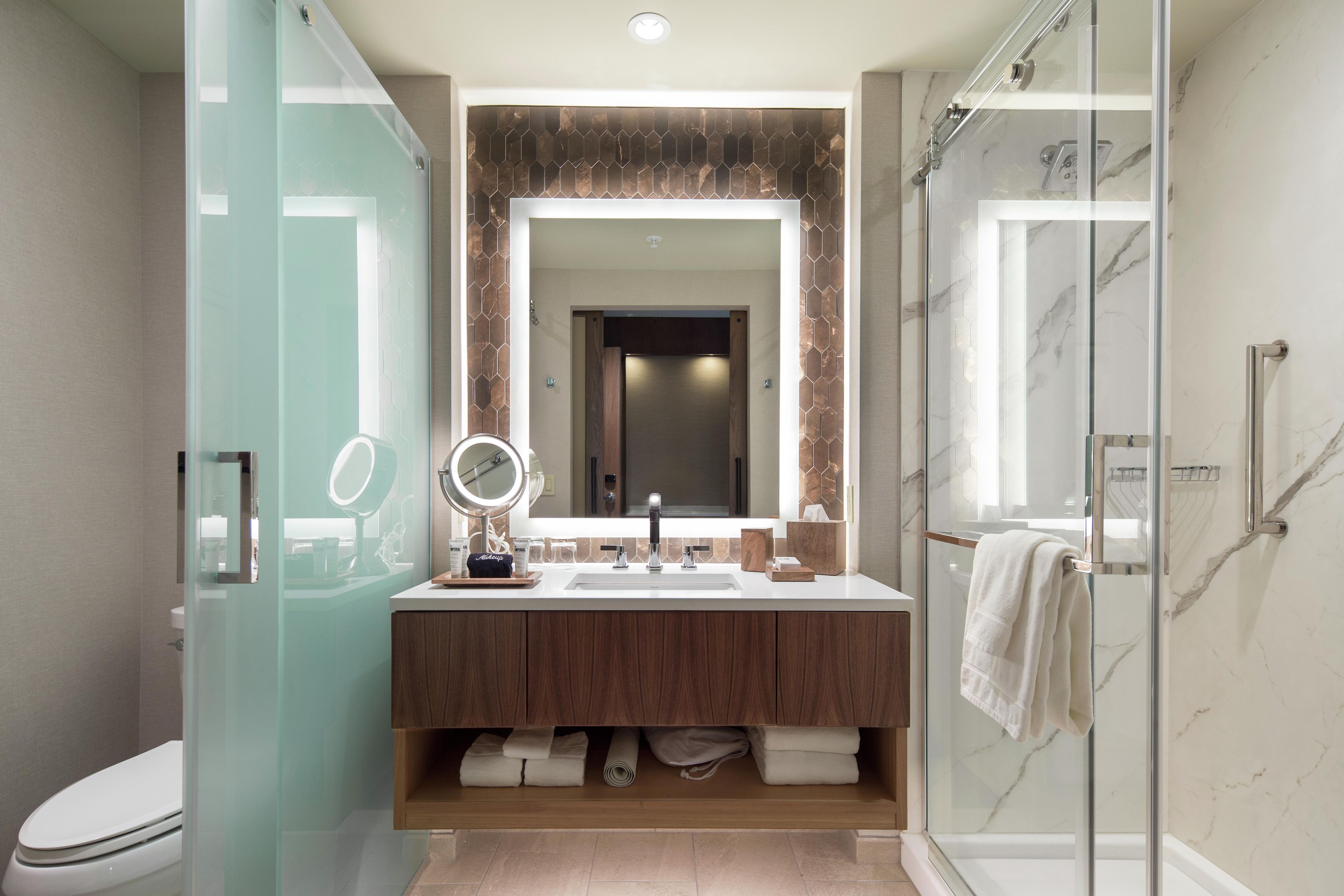 A modern bathroom with a glass-enclosed shower, a large mirror, and a vanity with a marble countertop.