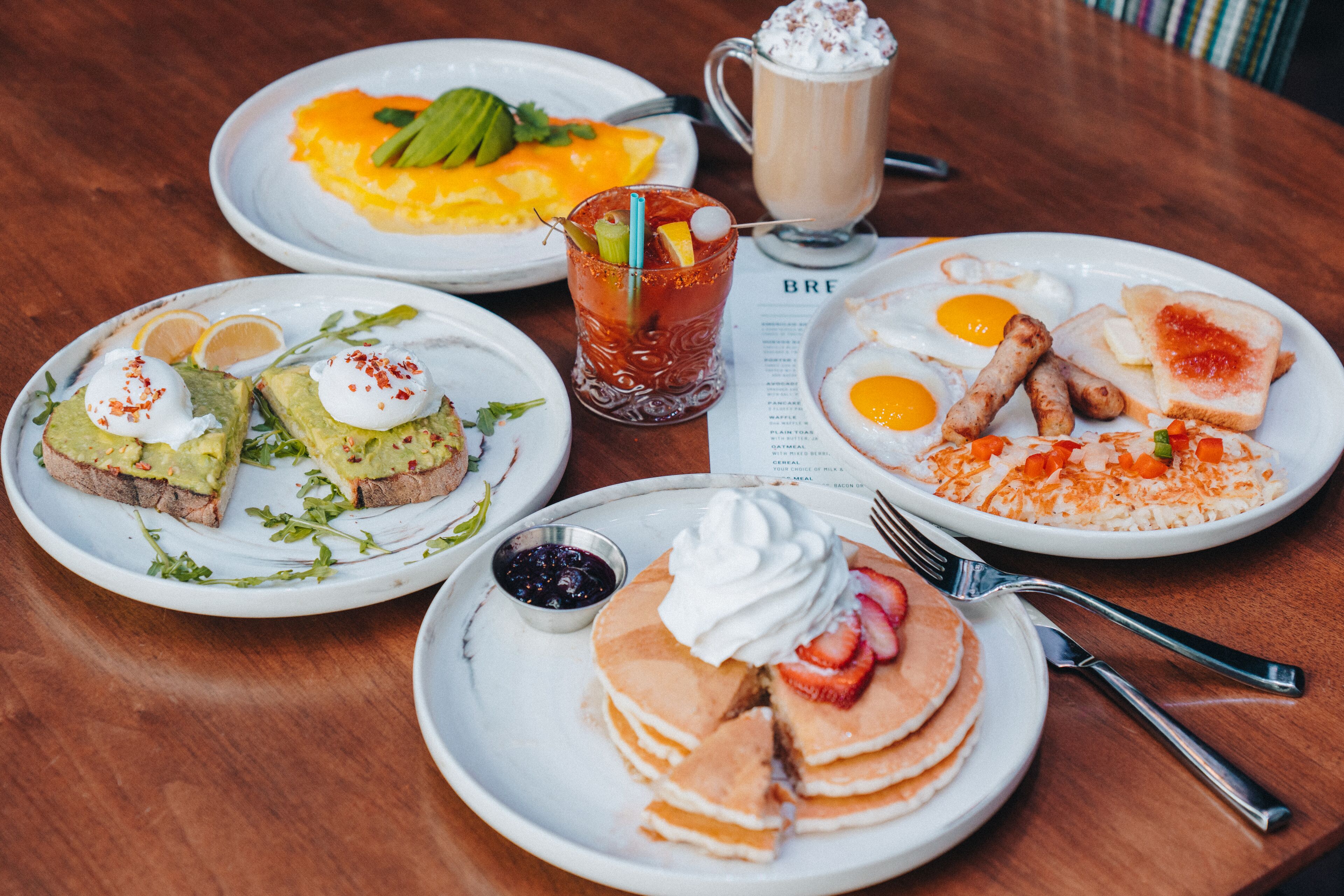 A breakfast setting with various dishes including pancakes, eggs, toast, and a beverage.