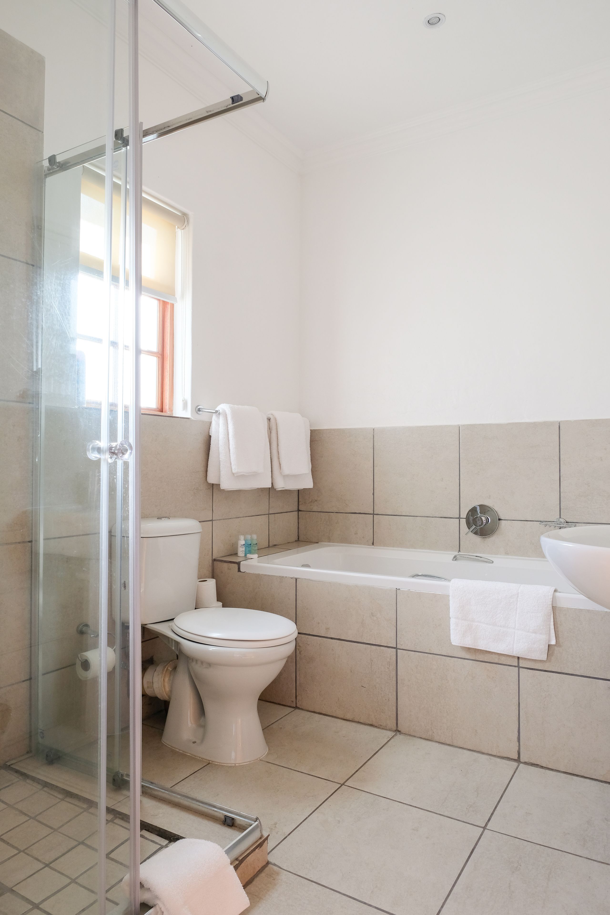 Et badeværelse med glasbrusekabine, toilet, badekar og vask.