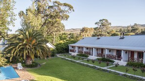 A two-story house with a swimming pool, a well-maintained lawn, and a view of the surrounding hills.