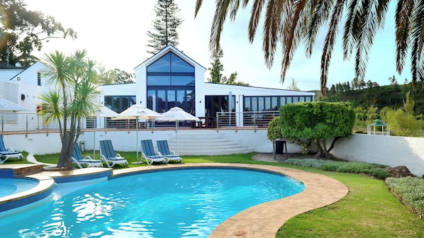 A modern house with a swimming pool, lounge chairs, and umbrellas.